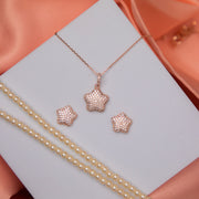 A rose gold-finish chunky star pendant set, displayed on a white surface with a satin background, including a pendant and a pair of earrings.